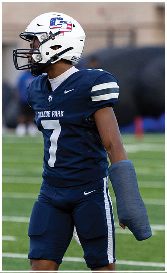 A person wearing a blue football uniform with the number seven and a helmet has their right arm in a blue cast while standing on a football field. Descripci n generada con IA