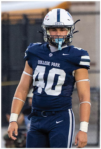 A person wearing a blue football uniform with the number 40 and the words College Park stands on a field with a helmet and mouthguard. Descripci n generada con IA