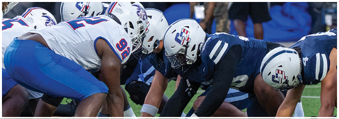 Two opposing American football teams in helmets and uniforms are lined up facing each other on the field, preparing for a play. Descripci n generada con IA