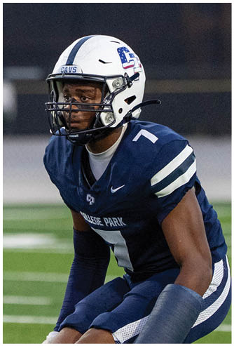 A person wearing a navy blue football uniform with the number seven and a white helmet is crouched on a football field. Descripci n generada con IA