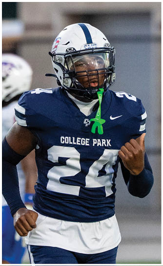 A person wearing a navy blue football uniform with the number 24 and the words College Park on the chest is on a field, wearing a white helmet with a blue stripe and a green mouthguard. Descripci n generada con IA