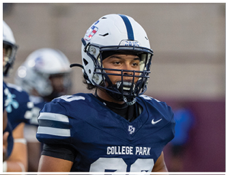 A person wearing a white football helmet and a navy blue jersey with “COLLEGE PARK" written on it is standing on a field with other players in the background. Descripci n generada con IA