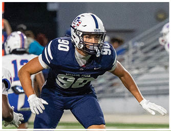 A person wearing a white football helmet and a navy blue jersey with “COLLEGE PARK" written on it is standing on a field with other players in the background. Descripci n generada con IA