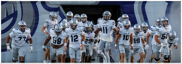 A group of people in sports uniforms run forward holding various flags while emerging from a tunnel. Descripci n generada con IA