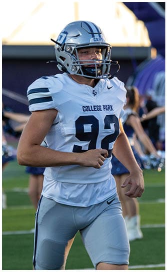 A person wearing a navy blue football uniform with the number 31 and a white helmet is standing on a football field with other players in the background. Descripci n generada con IA