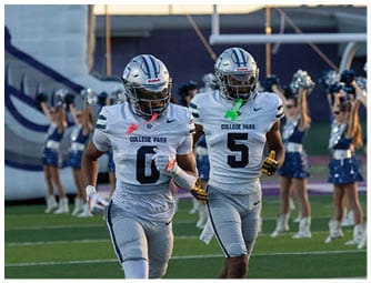 A person wearing a white football helmet with a blue stripe and the word “CAVS" on the front is on a football field with a scoreboard in the background. Descripci n generada con IA