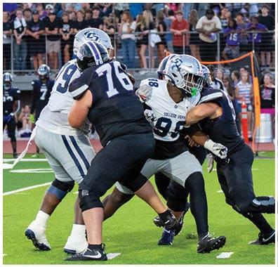 A person wearing a football uniform and helmet is crouched in a ready position on a green field with white yard lines. Descripci n generada con IA