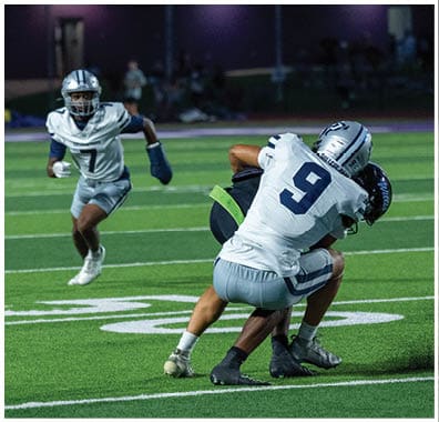 A person in a football uniform with a helmet and knee braces is crouched in a ready stance on a green field with white yard lines. Descripci n generada con IA