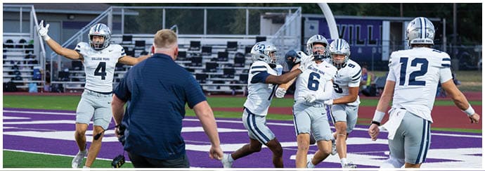 A person in a football uniform and helmet is on the field with blurred people and a banner reading “CFHS Brigade" in the background. Descripci n generada con IA
