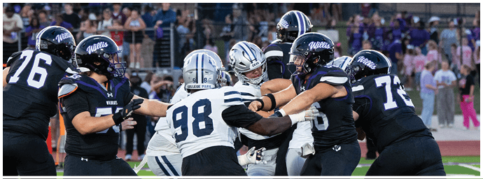 People in football uniforms are actively engaged in a play on a field with a crowd in the background. Descripci n generada con IA