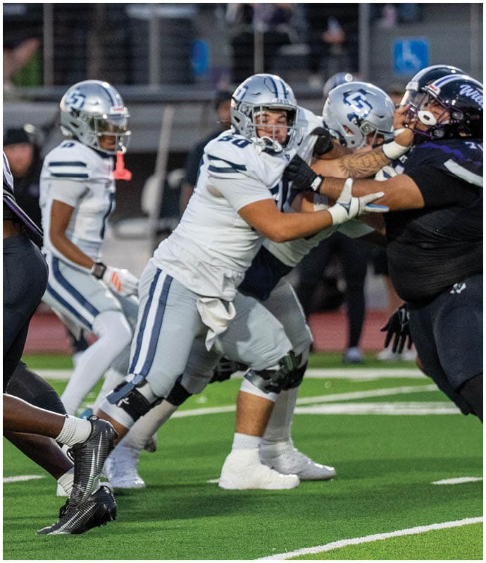 Two opposing American football teams are lined up at the line of scrimmage on a green field, preparing for the next play. Descripci n generada con IA
