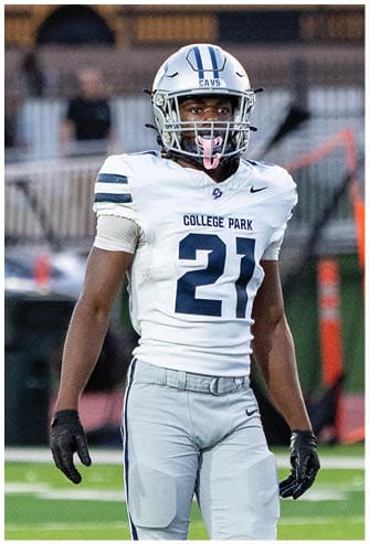 A person wearing a dark football jersey and a white helmet with a faceguard is on a football field. Descripci n generada con IA