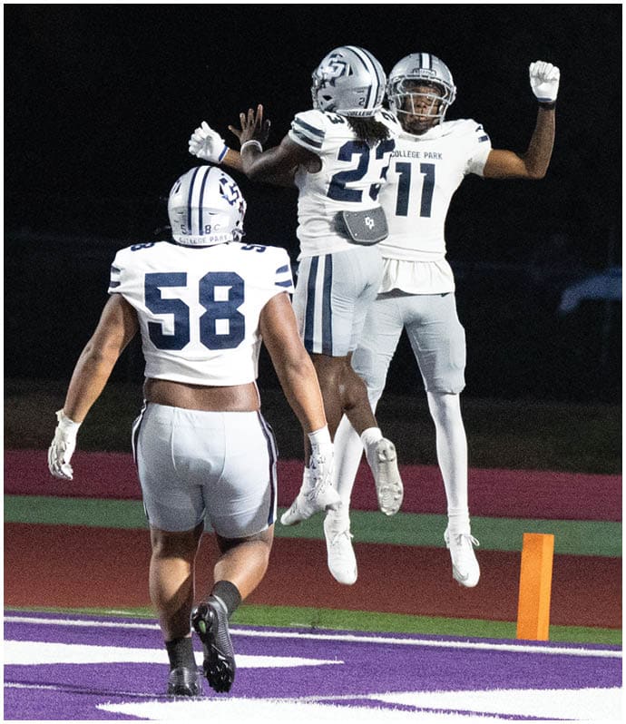 A person wearing a black football uniform with the number 80 is kicking a football on a green field with white yard lines. Descripci n generada con IA