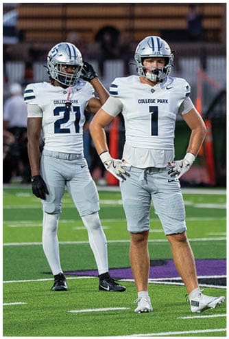 A person wearing a dark sports uniform and a white helmet is preparing to throw a football on a field. Descripci n generada con IA