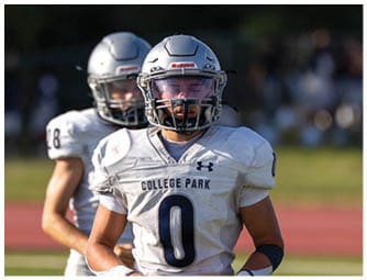 An adult wearing a backward cap adjusts the helmet of a person in a football uniform with the number seven on it during a practice or game. Descripci n generada con IA