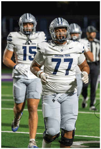A person wearing a blue and white football uniform and helmet is crouched on a field, appearing focused and ready for action. Descripci n generada con IA
