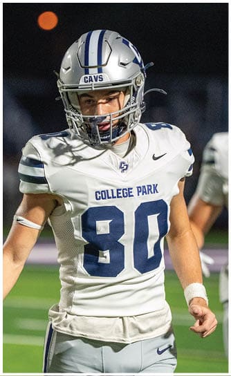 A person wearing a blue football uniform with the number seven and a helmet has their right arm in a blue cast while standing on a football field. Descripci n generada con IA