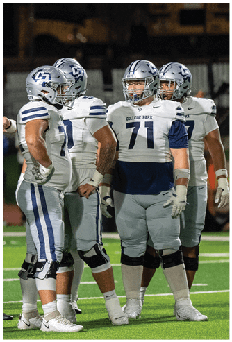 A person wearing a blue football uniform with the number 40 and the words College Park stands on a field with a helmet and mouthguard. Descripci n generada con IA