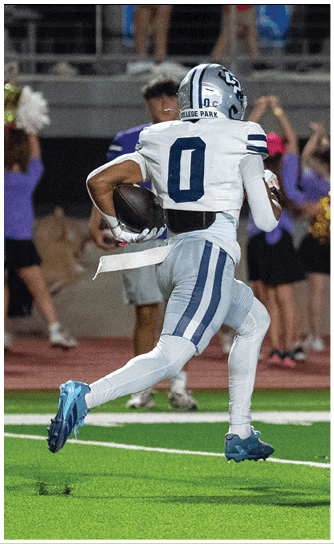Several people in football uniforms are engaged in a play on a green field with one person in a dark uniform holding the ball while others in white and blue uniforms attempt to block or tackle. Descripci n generada con IA