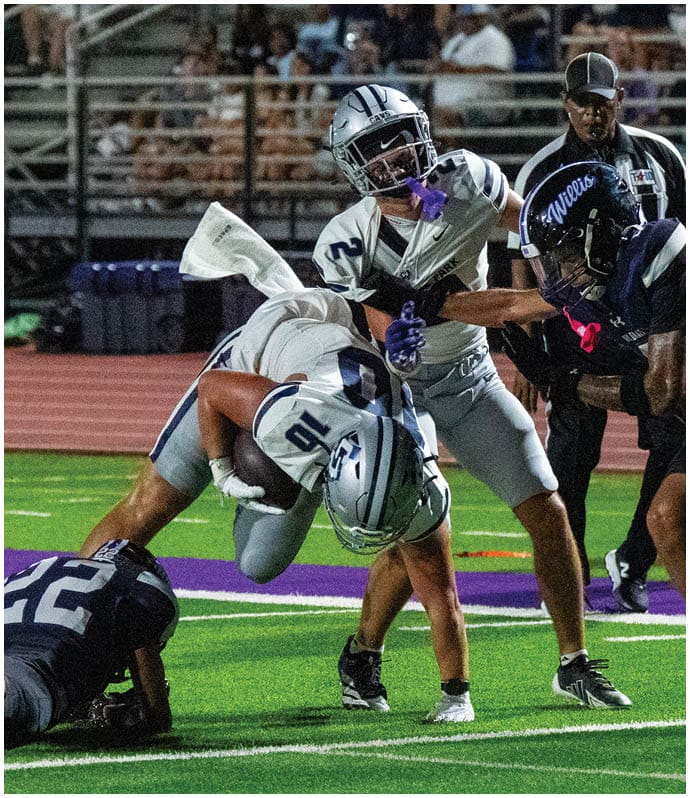 Two people wearing navy blue College Park football uniforms and white helmets stand side by side on a field. Descripci n generada con IA
