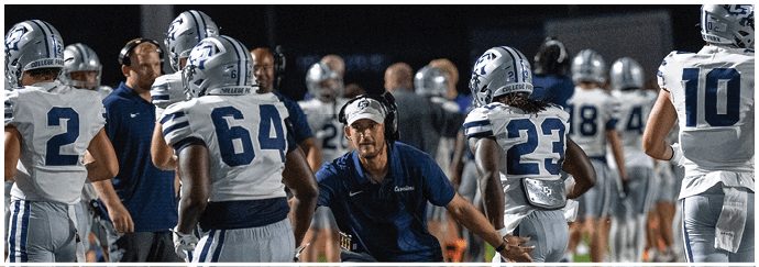 Two opposing American football teams in helmets and uniforms are lined up facing each other on the field, preparing for a play. Descripci n generada con IA