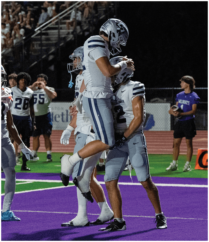 A person wearing a dark football uniform with the number 23 is running with the ball on a football field while other players in dark and white uniforms are nearby. Descripci n generada con IA