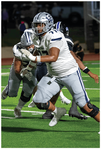 A person wearing a navy blue football uniform with the number seven and a white helmet is crouched on a football field. Descripci n generada con IA