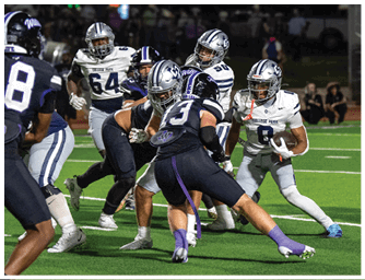 A person wearing a white football helmet and a navy blue jersey with “COLLEGE PARK" written on it is standing on a field with other players in the background. Descripci n generada con IA