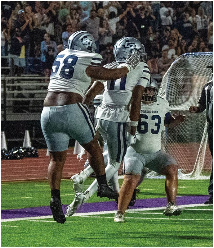 A person wearing a dark football uniform with the number 23 is running with the ball on a football field while other players in dark and white uniforms are nearby. Descripci n generada con IA