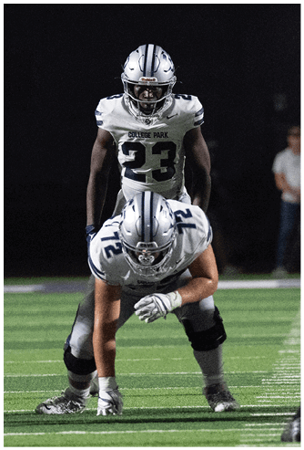 A person wearing a navy blue football uniform with the number seven and a white helmet is crouched on a football field. Descripci n generada con IA