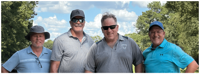 Four people wearing football helmets and white jerseys with “Bishop Verot" written on them stand side by side on a sports field with empty bleachers in the background. Descripci n generada con IA