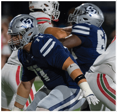 Two teams of football players in helmets and uniforms are engaged in a play on a green field during a game. Descripci n generada con IA