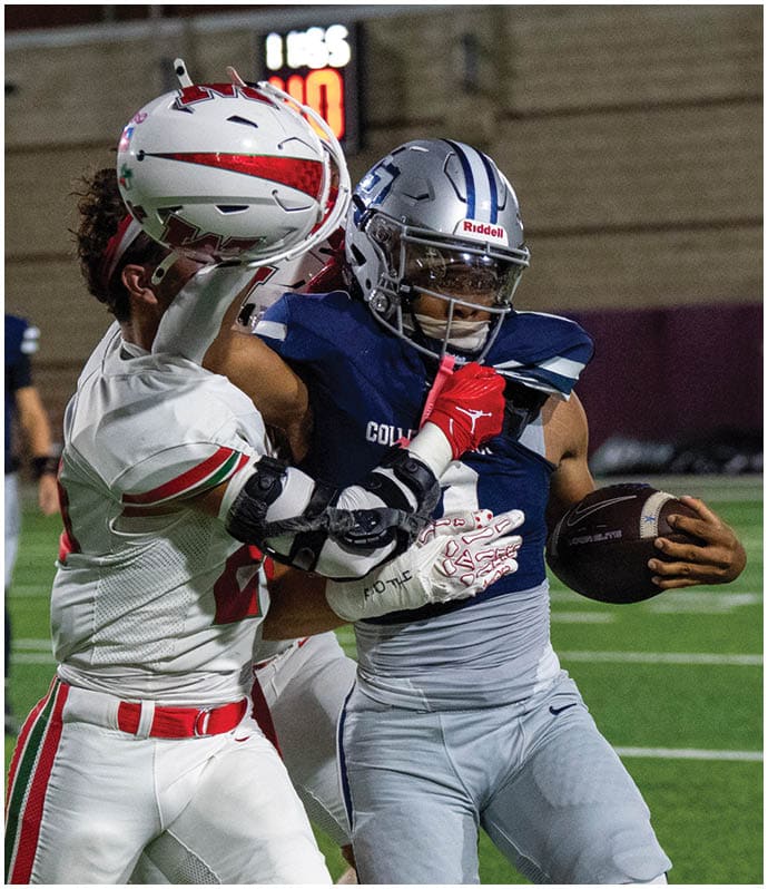 A person wearing a blue football uniform and helmet is holding a football while being tackled by another person in a white and red uniform on a football field. Descripci n generada con IA