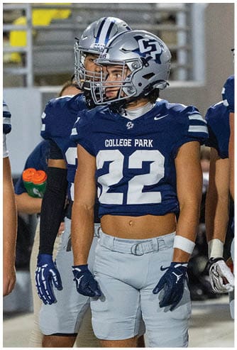 A person wearing a dark football jersey and a white helmet with a faceguard is on a football field. Descripci n generada con IA