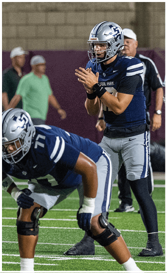 Three people in football uniforms and helmets are positioned on a field with one person standing behind the center preparing to receive the ball. Descripci n generada con IA