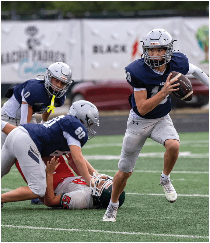 Three people in football uniforms are tackling a person in a different uniform who is lying on the ground during a game on a field. Descripci n generada con IA