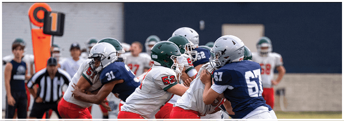 People wearing football helmets and uniforms are engaged in a close physical play on a football field with an official and a down marker visible in the background. Descripci n generada con IA