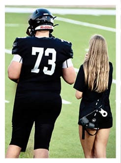 Two football players wearing black jerseys and holding hands. Description generated by AI