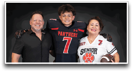 Three people stand together smiling with one wearing a football uniform and the others wearing casual clothing, one holding a football. Description generated by AI