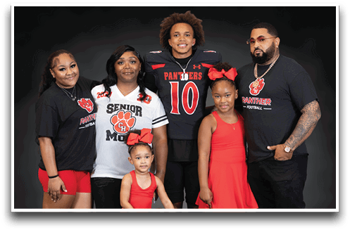 A group of six people including children and adults pose together smiling, with one person wearing a football uniform and others wearing matching team-themed clothing. Description generated by AI