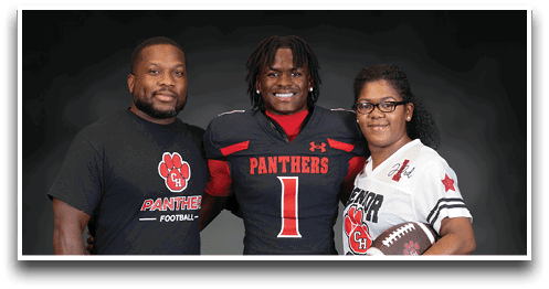 Three people stand together smiling with one wearing a football uniform and the others wearing shirts with a football team logo, one holding a football. Description generated by AI