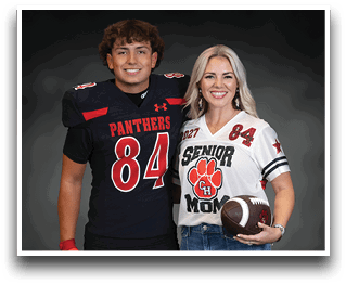 Two people smiling and standing side by side, one wearing a black football uniform with the number 84 and the other wearing a white “Senior Mom" jersey holding a football. Description generated by AI