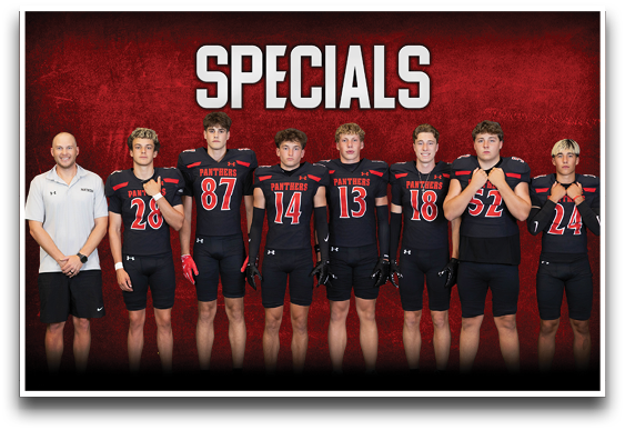 Seven people stand in a row against a red background with the word “SPECIALS" above them, six wearing black football uniforms with red and white accents and one in a white polo shirt and black shorts. Description generated by AI