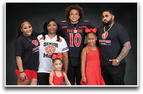 A group of six people including children and adults pose together smiling, with one person wearing a football uniform and others wearing matching team-themed clothing. Description generated by AI