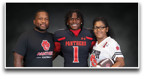 Three people stand together smiling with one wearing a football uniform and the others wearing shirts with a football team logo, one holding a football. Description generated by AI