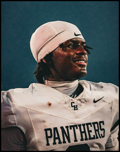 A person wearing a white football uniform with the word Panthers and a white head covering is looking to the side with a slight smile against a dark background. Description generated by AI