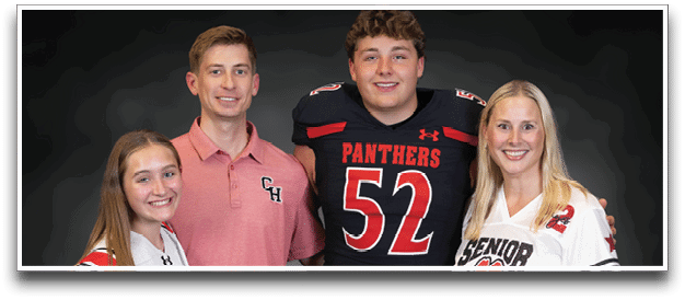 Four people wearing sports jerseys and holding footballs stand together smiling against a dark background. Description generated by AI