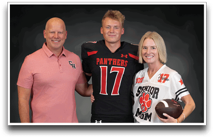 Three adults stand together smiling with one wearing a black sports jersey with the number 17 and the word Panthers, another in a pink polo shirt, and the third in a white sports jersey holding a football with the words Senior Mom. Description generated by AI