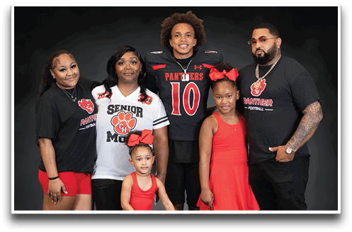 A group of six people including children and adults pose together smiling, with one person wearing a football uniform and others wearing matching team-themed clothing. Description generated by AI