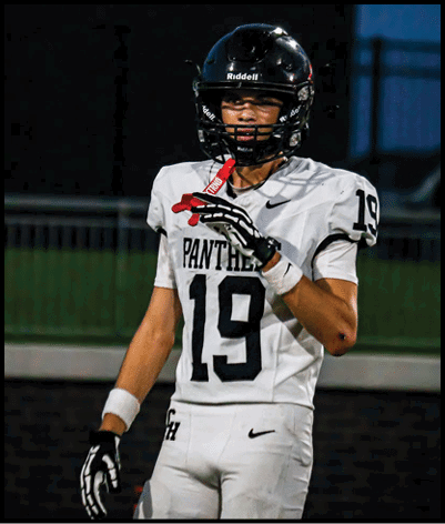 A person wearing a white football jersey with the number 19 and a black helmet is standing on a field at dusk. Description generated by AI